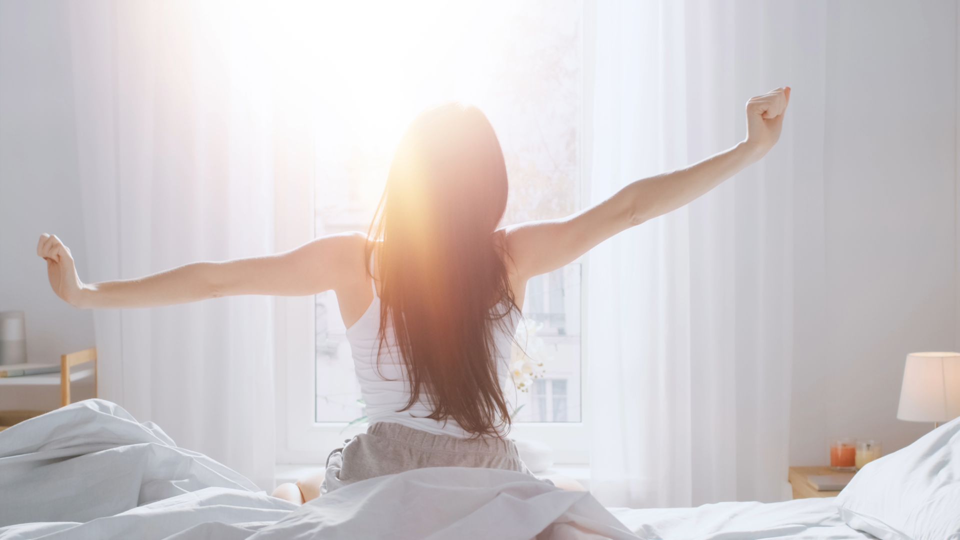 Woman stretching in bed with sunlight streaming through a window. Single Origin Club.